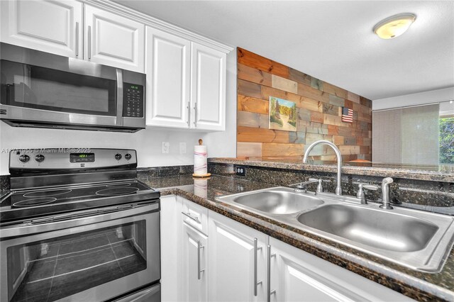 kitchen featuring appliances with stainless steel finishes, white cabinetry, sink, dark tile patterned floors, and kitchen peninsula