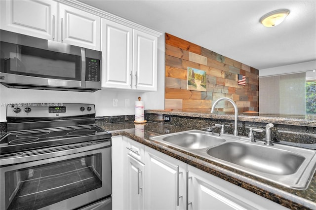 kitchen featuring a sink, white cabinets, appliances with stainless steel finishes, backsplash, and dark stone counters