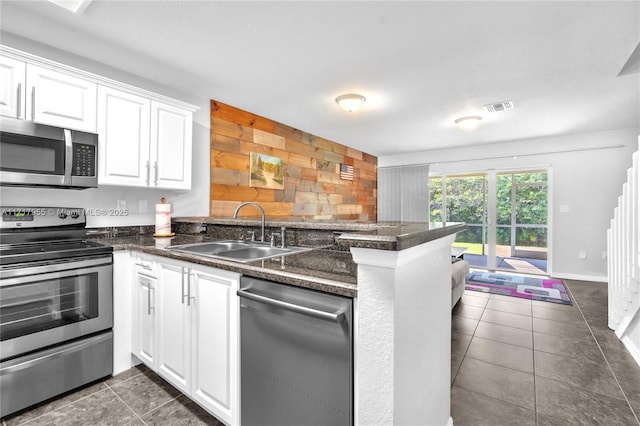 kitchen featuring sink, dark tile patterned floors, appliances with stainless steel finishes, white cabinetry, and kitchen peninsula