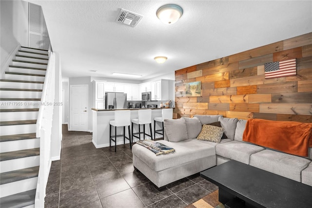 living room with stairs, a textured ceiling, visible vents, and wooden walls