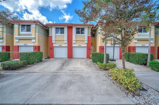 townhome / multi-family property with a garage, a tile roof, driveway, and stucco siding