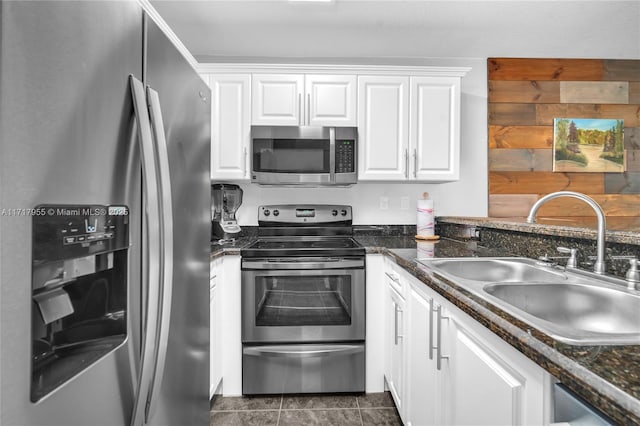 kitchen with sink, white cabinetry, appliances with stainless steel finishes, dark tile patterned floors, and dark stone counters