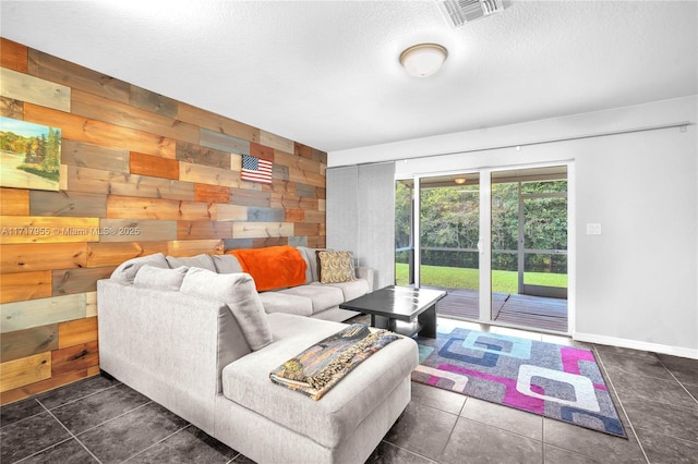 living room featuring a textured ceiling, dark tile patterned floors, wood walls, visible vents, and baseboards