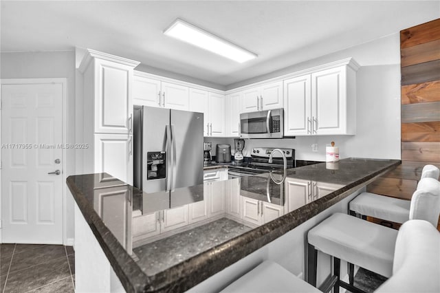 4923 SW 66th Ter Unit 4923, Davie, FL 33314 - kitchen with dark stone countertops, appliances with stainless steel finishes, a kitchen bar, white cabinetry, and a peninsula