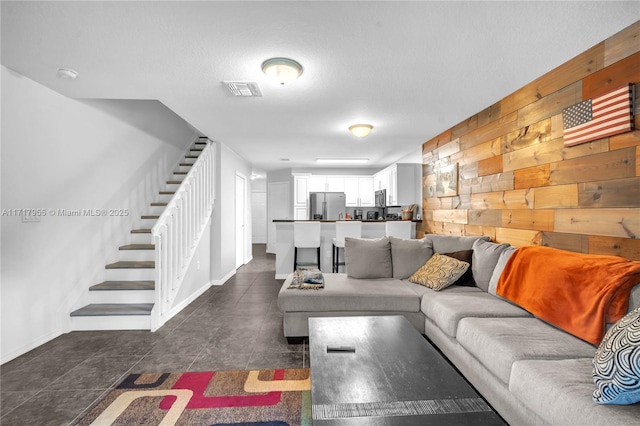 living room featuring wood walls, stairs, and visible vents