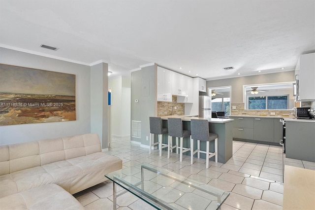 kitchen featuring white cabinets, a breakfast bar, freestanding refrigerator, gray cabinets, and light countertops