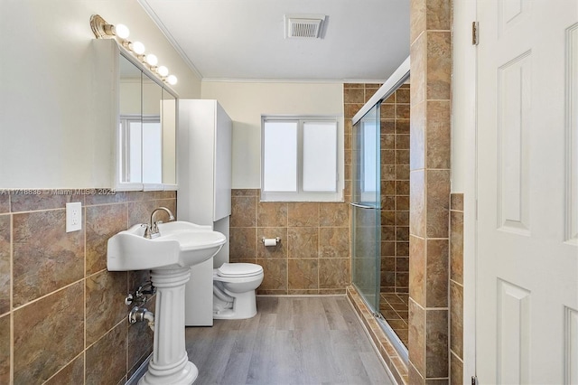 bathroom with visible vents, toilet, crown molding, a shower stall, and tile walls