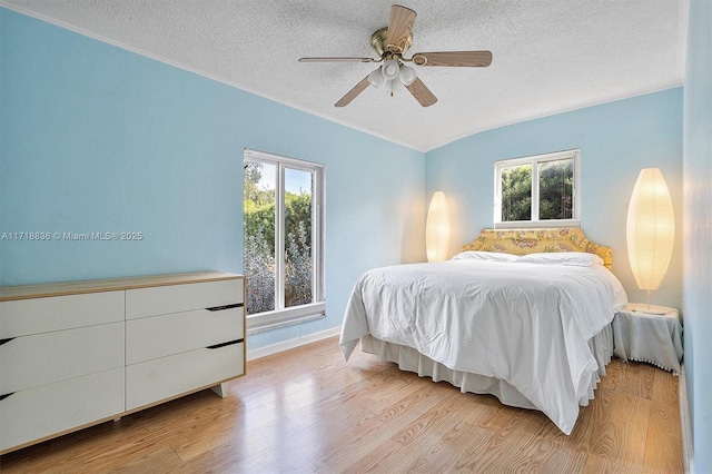 bedroom with a textured ceiling, ceiling fan, multiple windows, and light wood-type flooring