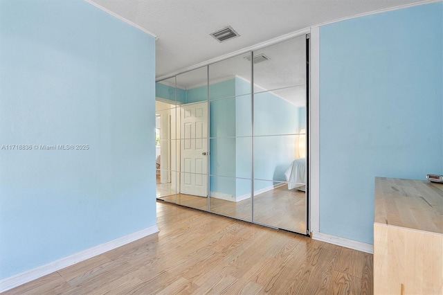 unfurnished bedroom featuring light wood finished floors, baseboards, visible vents, and a closet