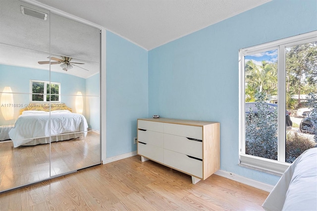 bedroom with light wood finished floors, lofted ceiling, visible vents, a textured ceiling, and baseboards