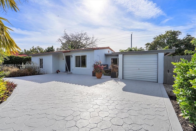 ranch-style house with concrete driveway, a tiled roof, an attached garage, fence, and stucco siding