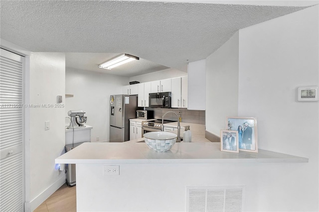 kitchen featuring a textured ceiling, white cabinetry, kitchen peninsula, and stainless steel appliances