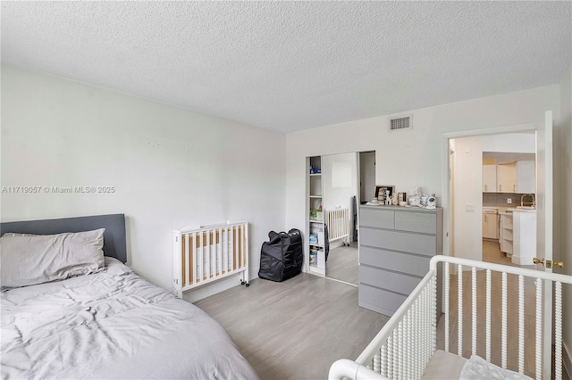 bedroom with ensuite bathroom, light hardwood / wood-style flooring, and a textured ceiling