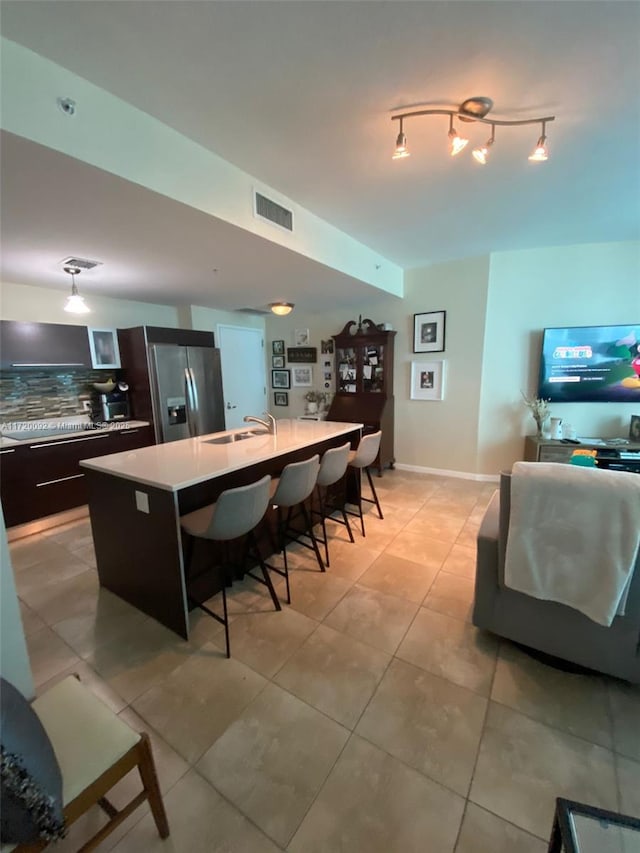 kitchen featuring sink, stainless steel refrigerator with ice dispenser, backsplash, a breakfast bar area, and a kitchen island with sink