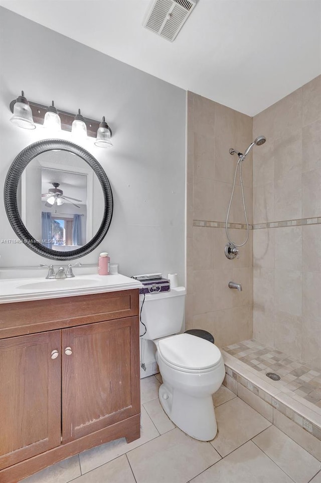 bathroom with toilet, tile patterned floors, vanity, ceiling fan, and a tile shower