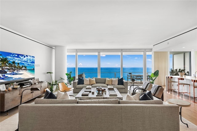 living room featuring a water view, light wood-type flooring, and a wall of windows