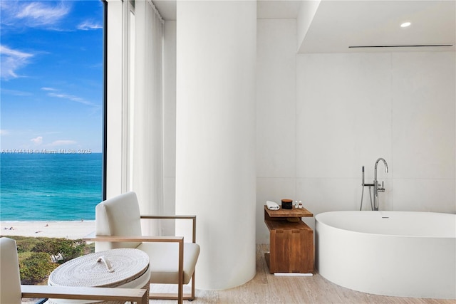 bathroom featuring hardwood / wood-style flooring, a water view, a tub, and a view of the beach