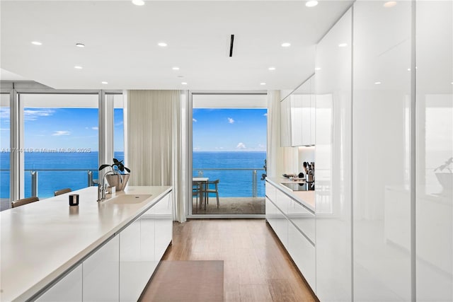 kitchen featuring light wood-type flooring, sink, a water view, white cabinetry, and plenty of natural light