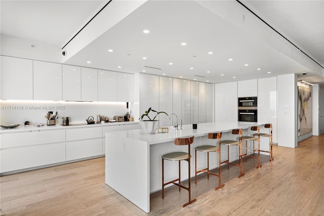 kitchen with a kitchen breakfast bar, black double oven, a spacious island, light hardwood / wood-style flooring, and white cabinetry