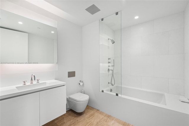 full bathroom featuring hardwood / wood-style flooring, tiled shower / bath combo, toilet, and vanity