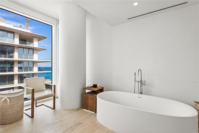 bathroom featuring floor to ceiling windows, a bathtub, a water view, and hardwood / wood-style floors