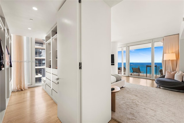 hallway featuring light wood-type flooring, a water view, and a wall of windows