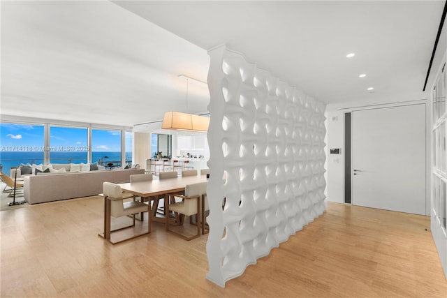 dining space with floor to ceiling windows, a water view, and light wood-type flooring