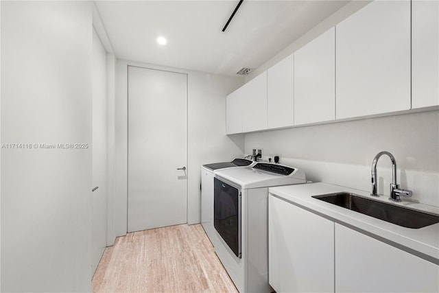 laundry room with cabinets, light wood-type flooring, washer and dryer, and sink