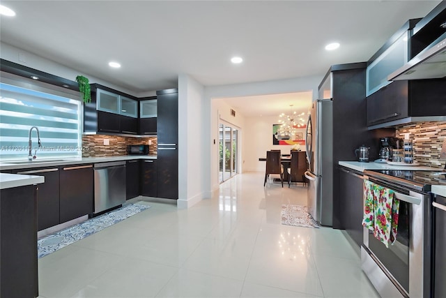 kitchen featuring sink, wall chimney exhaust hood, backsplash, light tile patterned flooring, and appliances with stainless steel finishes