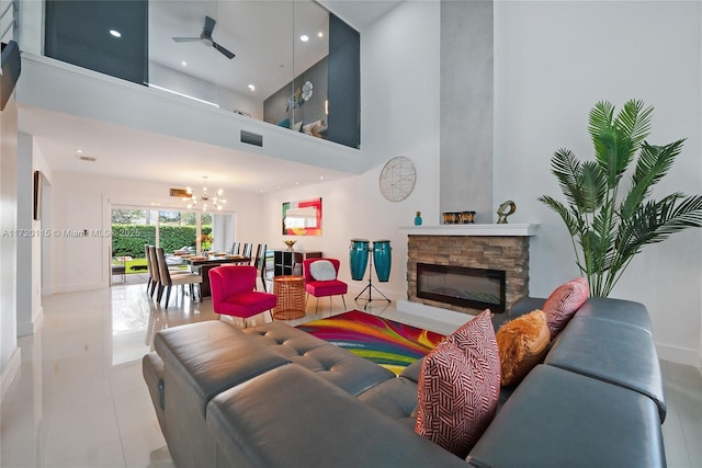 living room with a stone fireplace, light tile patterned floors, ceiling fan with notable chandelier, and a high ceiling