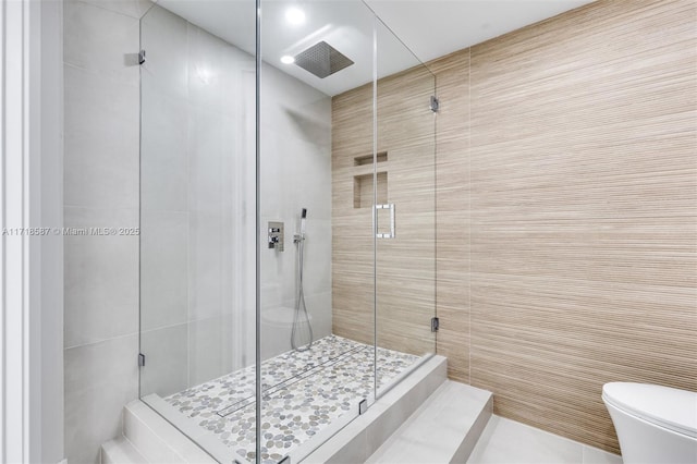 bathroom with tile patterned floors, toilet, a shower with door, and tile walls