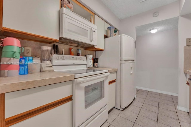 kitchen featuring white cabinets, light tile patterned floors, white appliances, and a textured ceiling