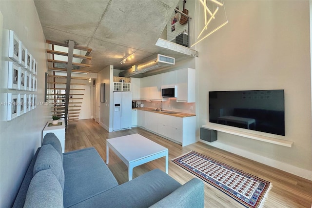 living room with a towering ceiling, light hardwood / wood-style floors, and sink
