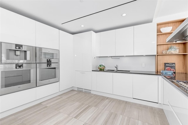 kitchen featuring island exhaust hood, white cabinetry, sink, and stainless steel double oven