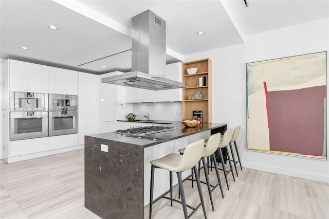 kitchen featuring kitchen peninsula, a kitchen breakfast bar, island range hood, stainless steel appliances, and white cabinetry