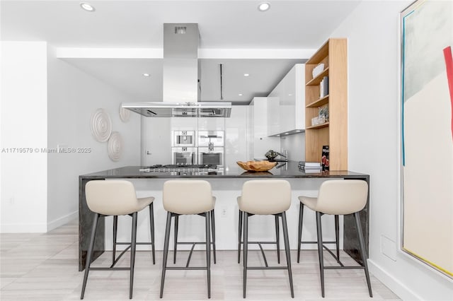 kitchen featuring stainless steel gas stovetop, a breakfast bar, white cabinetry, kitchen peninsula, and island exhaust hood