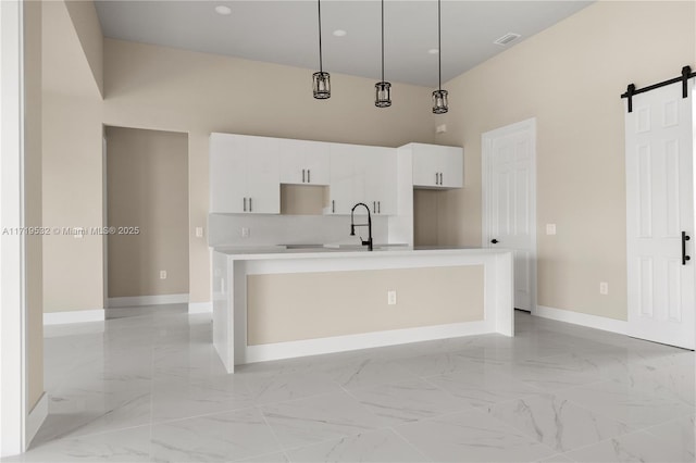 kitchen featuring sink, a barn door, decorative light fixtures, a center island with sink, and white cabinetry