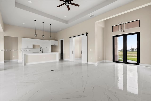 unfurnished living room featuring ceiling fan, sink, a high ceiling, a raised ceiling, and a barn door