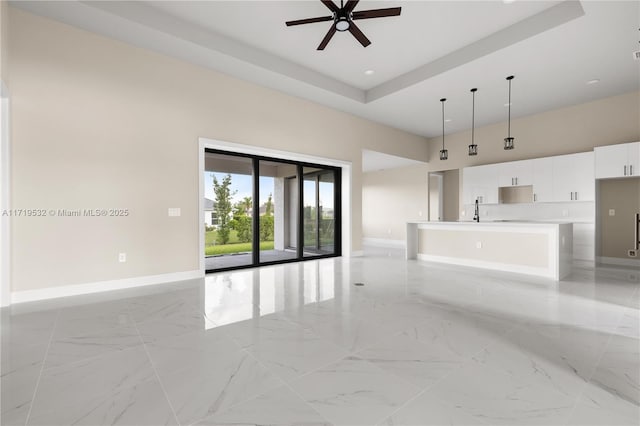 unfurnished living room with a raised ceiling, ceiling fan, and sink