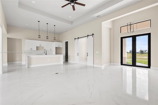 unfurnished living room featuring a raised ceiling, sink, ceiling fan, a barn door, and a towering ceiling