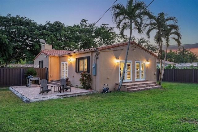 back house at dusk with a lawn and a patio area