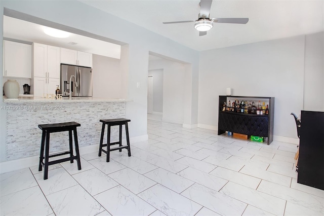 kitchen with a kitchen breakfast bar, stainless steel fridge with ice dispenser, kitchen peninsula, ceiling fan, and white cabinetry