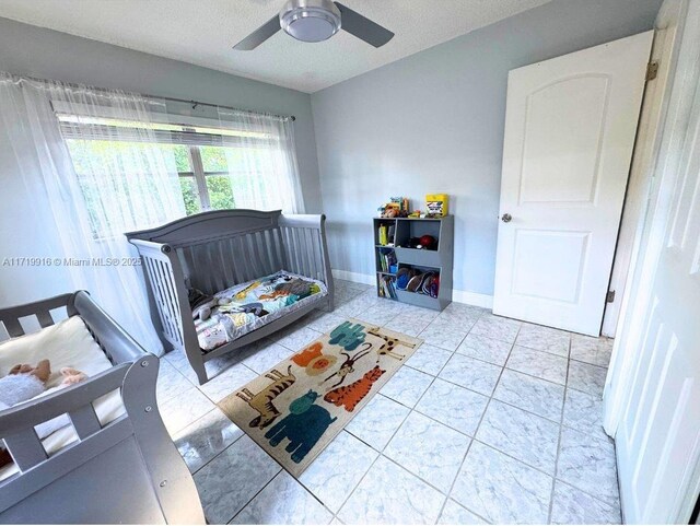 bedroom with ceiling fan, a crib, multiple windows, and light tile patterned floors