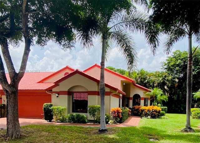 mediterranean / spanish-style house with a garage, a tiled roof, concrete driveway, stucco siding, and a front lawn