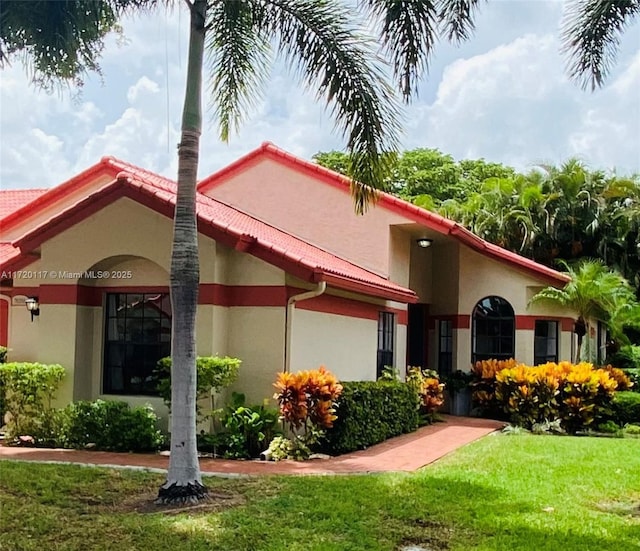 view of front of house featuring a tiled roof, a front lawn, and stucco siding