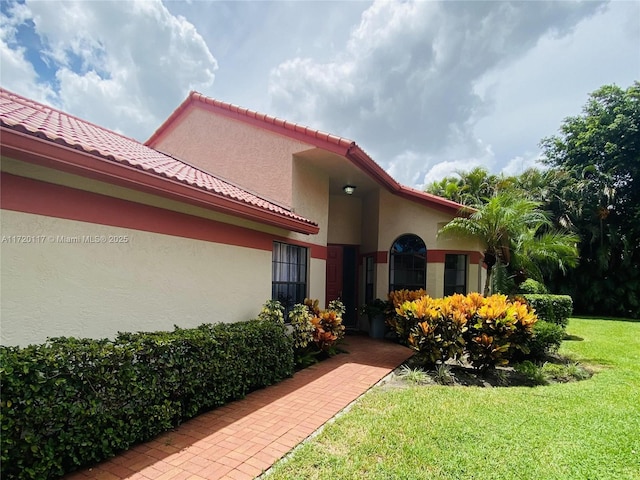 exterior space with a yard, a tile roof, and stucco siding