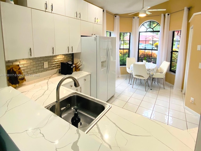 kitchen featuring tasteful backsplash, white refrigerator with ice dispenser, white cabinets, light stone counters, and sink