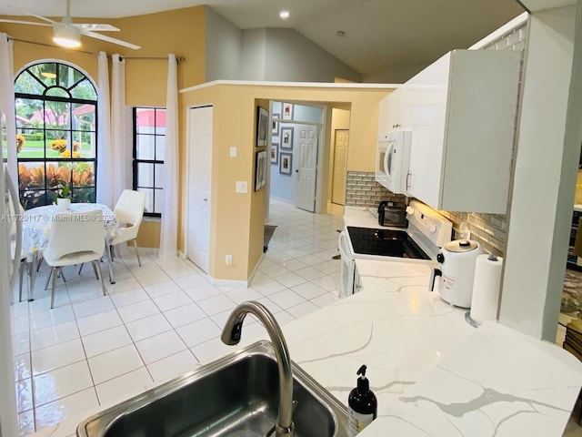 kitchen with stove, sink, light tile patterned flooring, white cabinets, and light stone counters