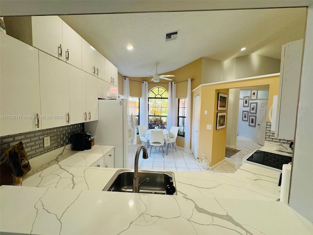 kitchen with a textured ceiling, white cabinetry, white fridge, sink, and ceiling fan