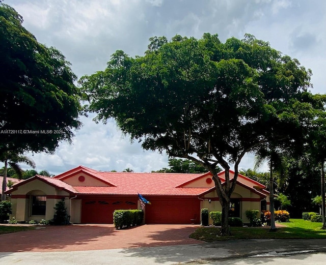 ranch-style house with an attached garage, stucco siding, decorative driveway, and a tiled roof